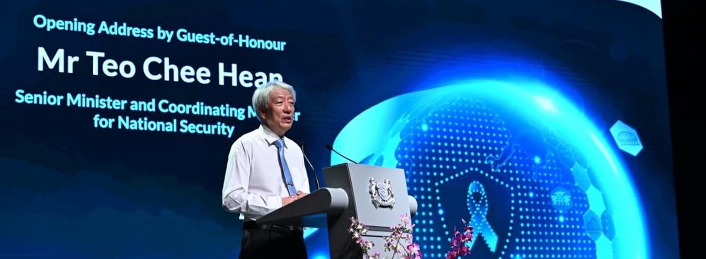 Teo Chee Hean speaking behind lectern with Singapore coat of arms, digital display behind.